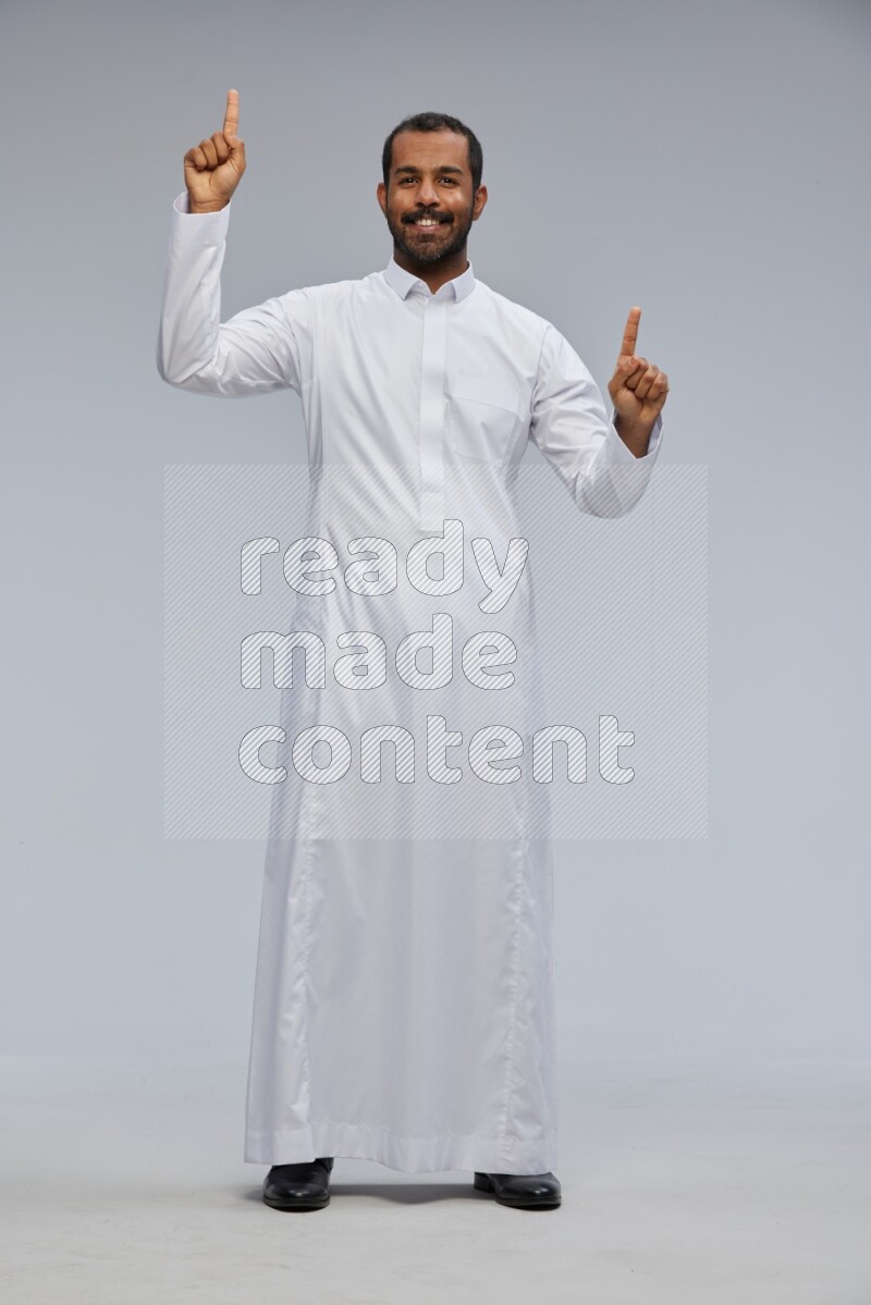 Saudi man Wearing Thob standing interacting with the camera on Gray background