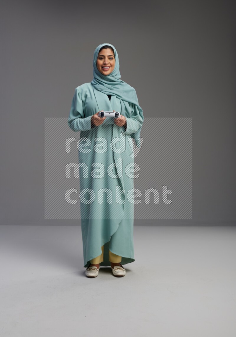 Saudi Woman wearing Abaya standing Playing Games on Gray background