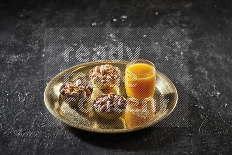 Nuts in metal bowls with qamar eldin on a tray in dark setup