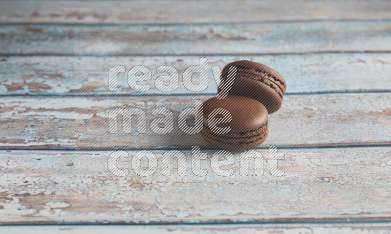 45º Shot of two Brown Dark Chocolate macarons on light blue wooden background