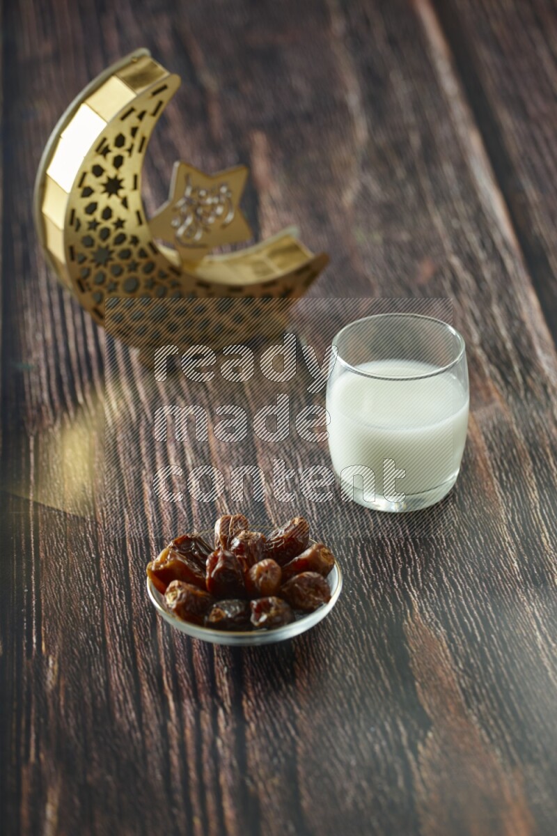 A wooden golden crescent lantern with different drinks, dates, nuts, prayer beads and quran on brown wooden background