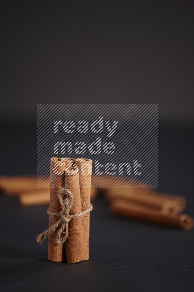 4 Cinnamon sticks stacked and bounded with more sticks in the background on black flooring