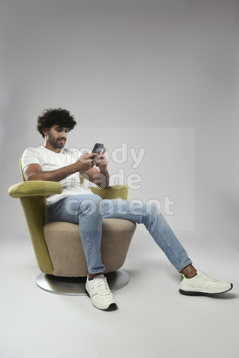 A man wearing casual sitting on a chair texting on the phone on white background
