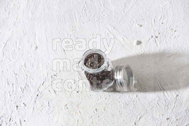 A glass spice jar full of cloves on textured white flooring