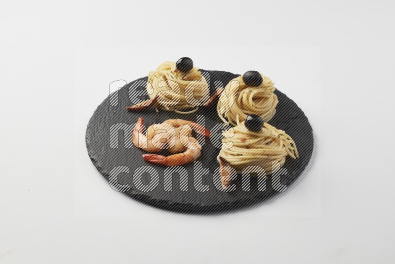 spaghetti nests with white sauce and shrimp on a black slate on a white background