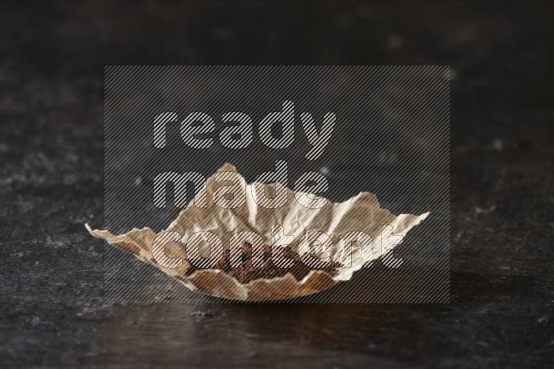 Cloves powder in crumpled piece of paper on a textured black flooring