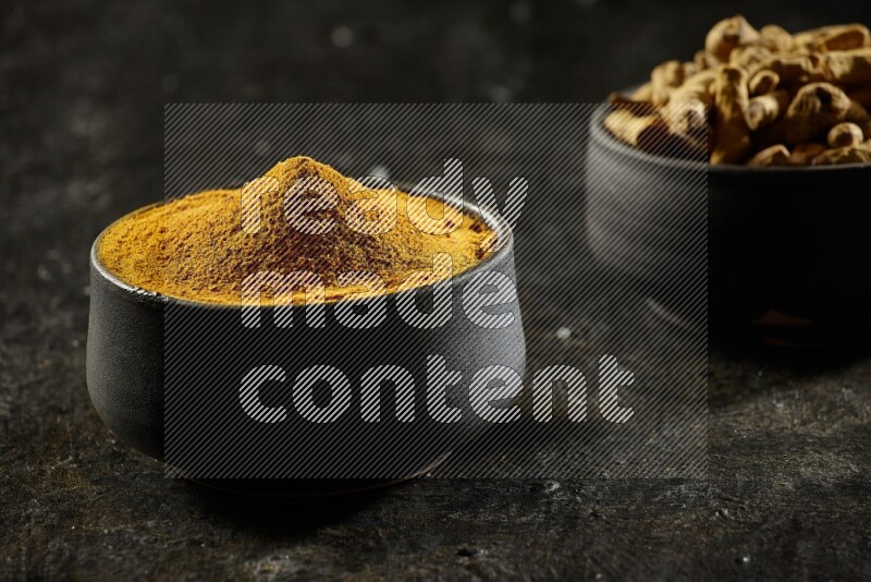 وعاءان من الفخار باللون الأسود، أحدهما ممتلئ ببودرة الكركم والآخر ممتلئ بأصابع كاملة من الكركم المجفف على خلفية سوداء