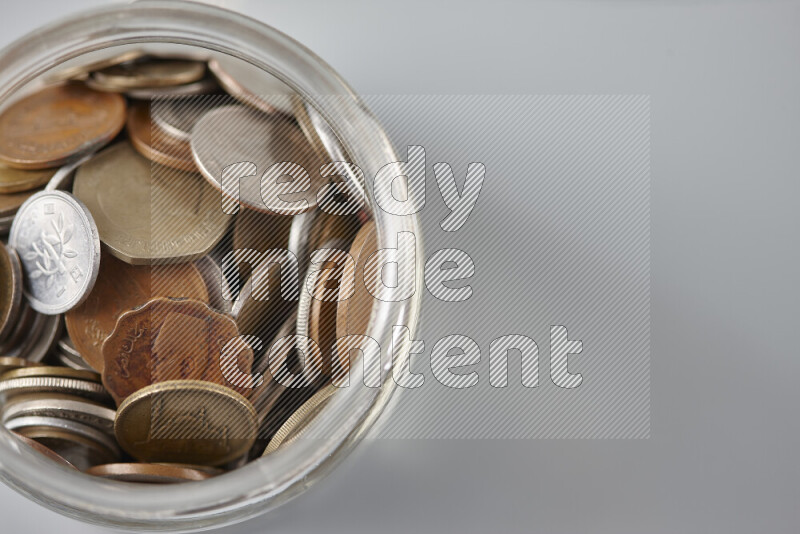 Random old coins in a glass jar on grey background