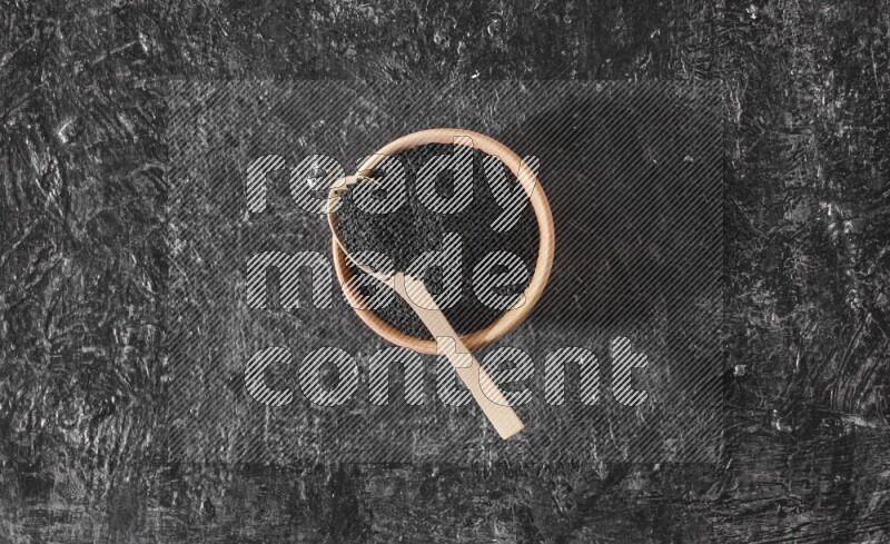 وعاء خشبي مع ملعقة خشبية ممتلئان ببذور حبة البركة علي خلفية سوداء