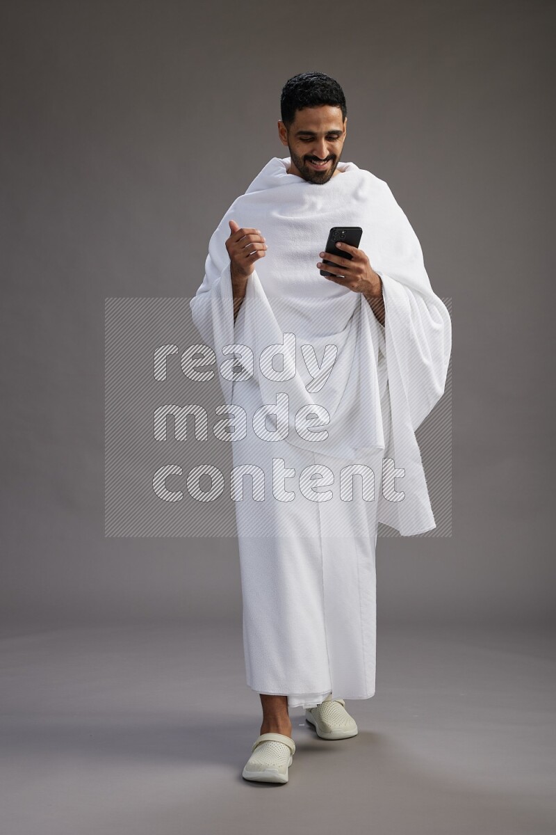 A man wearing Ehram Standing texting on phone on gray background