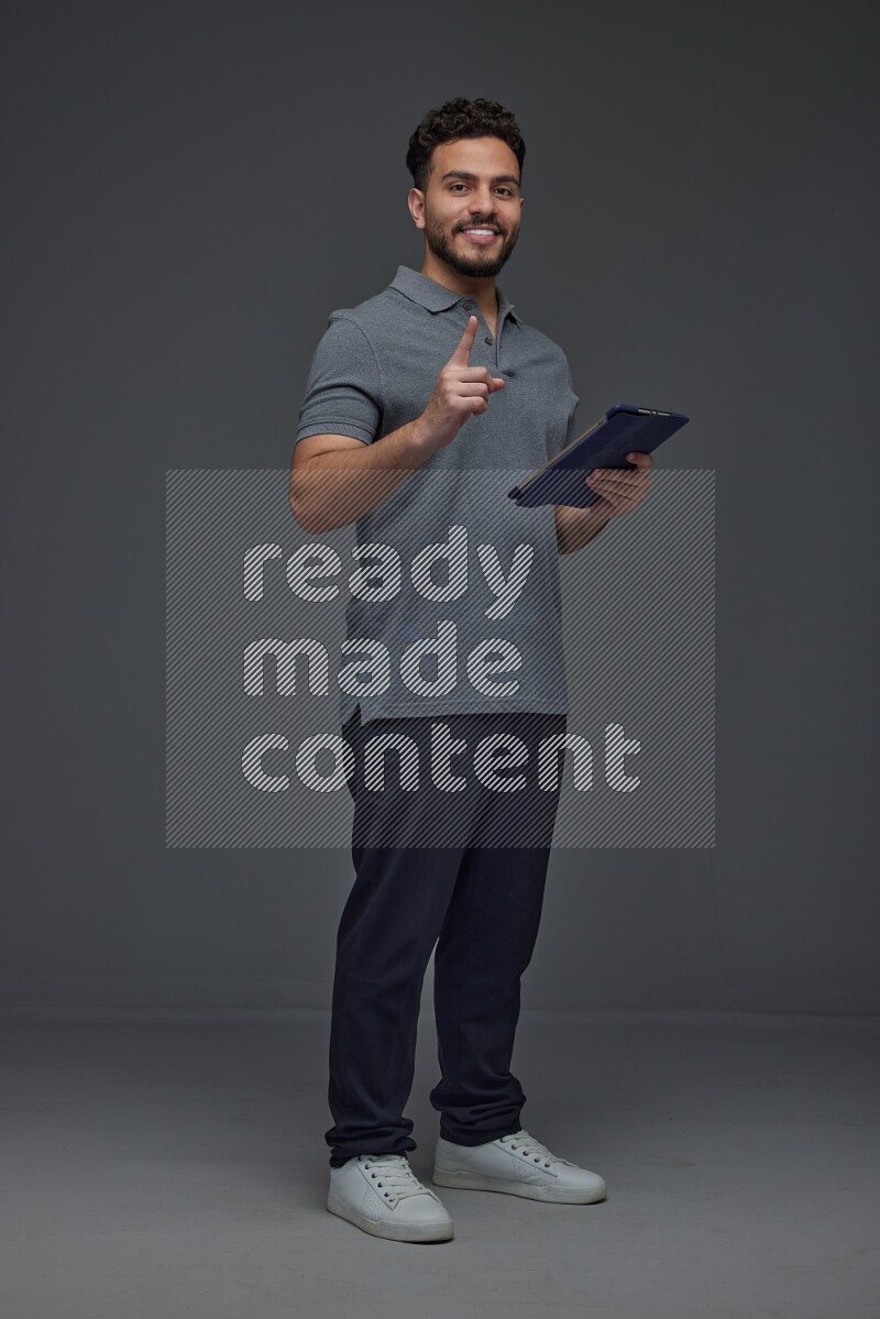 A man wearing casual standing and using his tablet and making multi hand gestures different angles eye level on a gray background