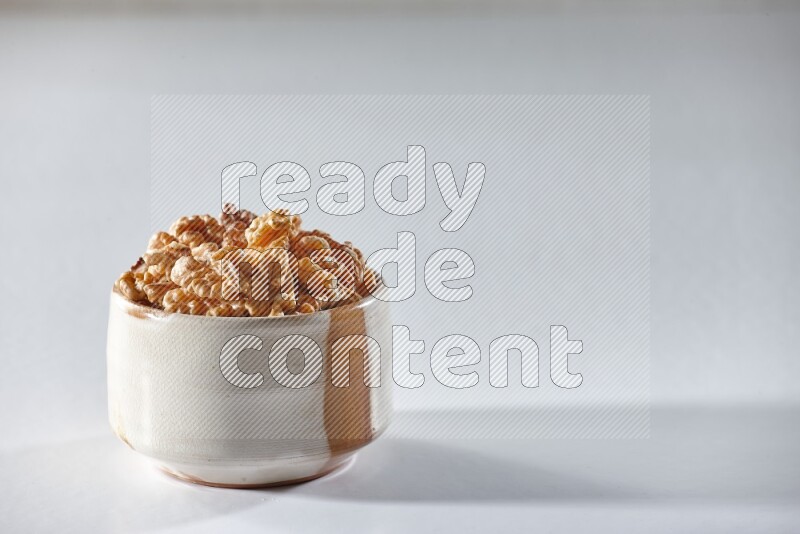 A beige ceramic bowl full of peeled walnuts on a white background in different angles