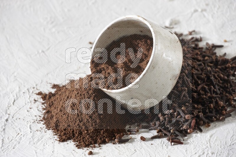 A beige ceramic bowl with cloves powder spilled out of it on a textured white flooring