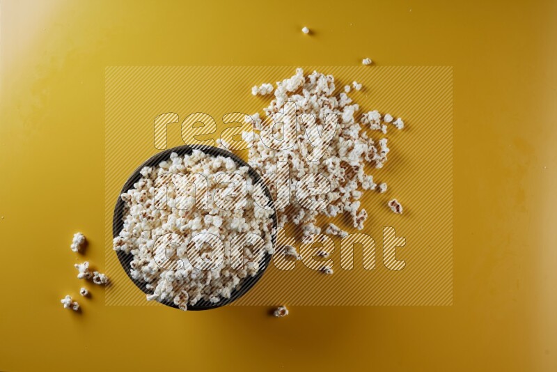 A copper ceramic bowl full of popcorn with popcorn beside it on a yellow background in different angles