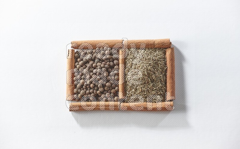 مربعان من أعواد القرفة ممتلئان ببهار الفلفل الحلو والكمون علي خلفية بيضاء