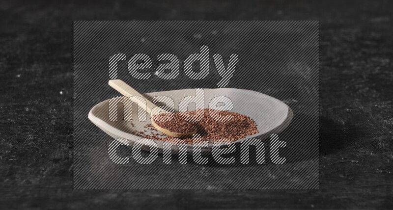 A multicolored pottery plate full of garden cress seeds and wooden spoon full of seeds on a textured black flooring