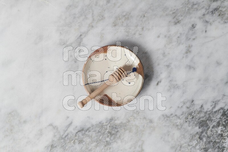 Multicolored pottery plate with wooden honey dipper in it on grey marble background