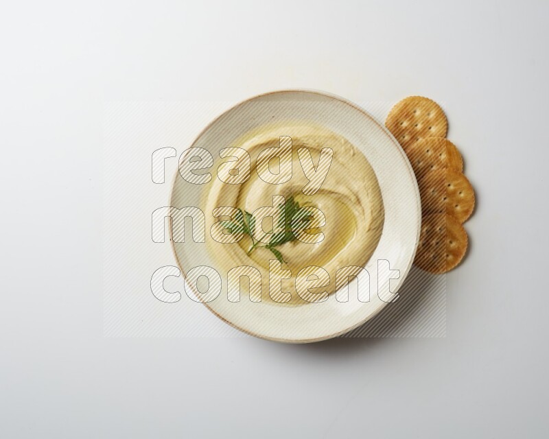 Hummus in a pottry plate garnished with parsley on a white back ground