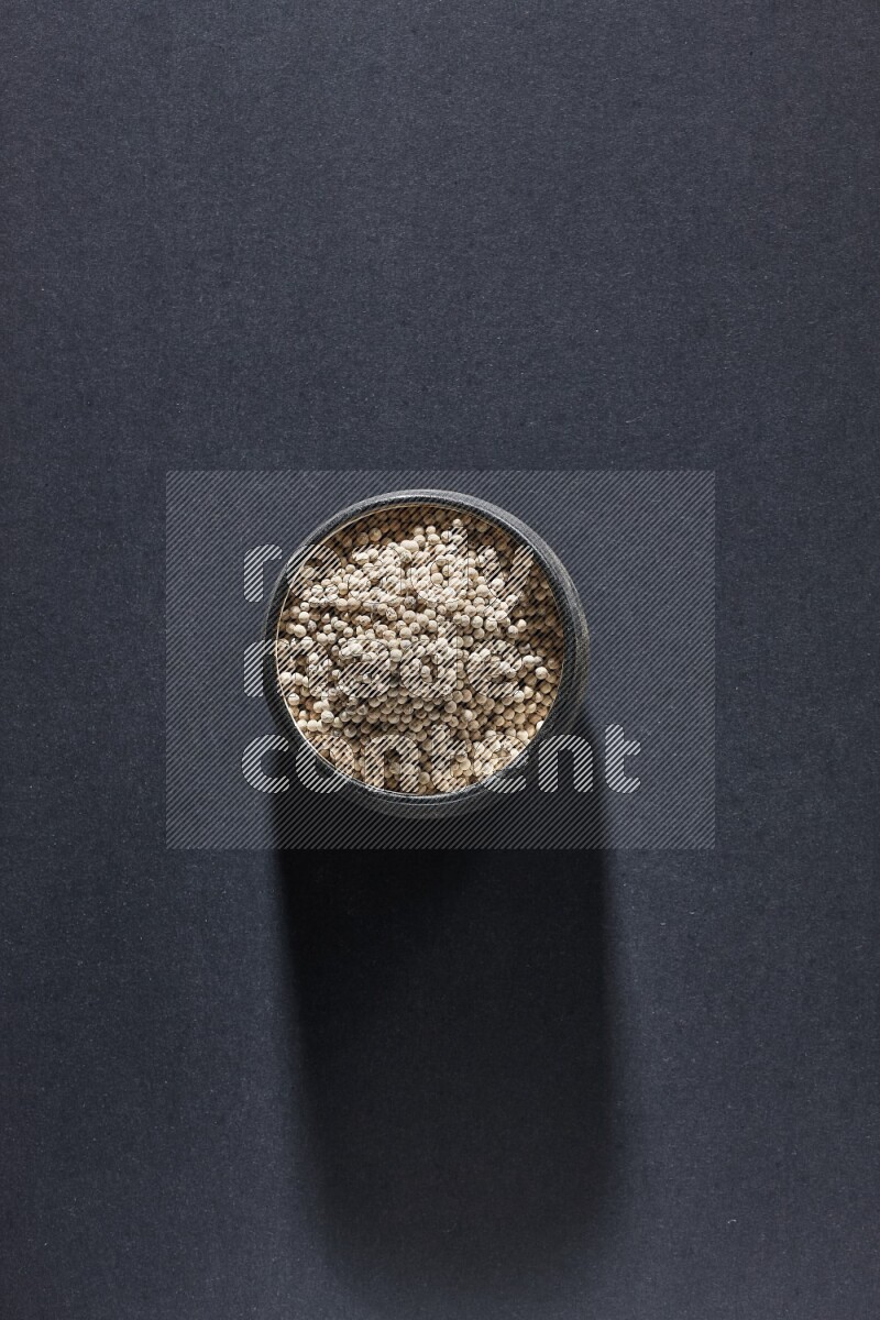 Black pottery bowl full of white pepper on black flooring