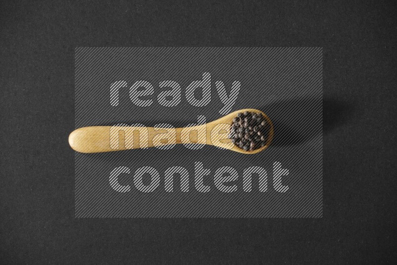 A wooden spoon full of black pepper on a black flooring