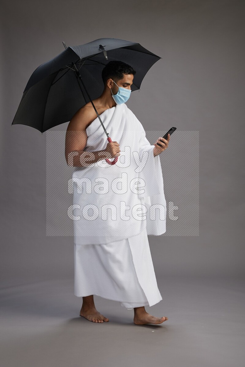 A man wearing Ehram and mask Standing holding umbrella on gray background on gray background