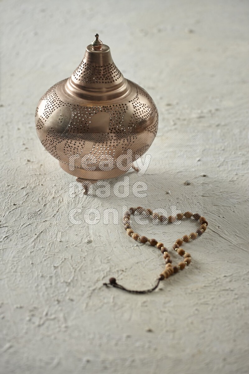 A golden lantern with different drinks, dates, nuts, prayer beads and quran on textured white background