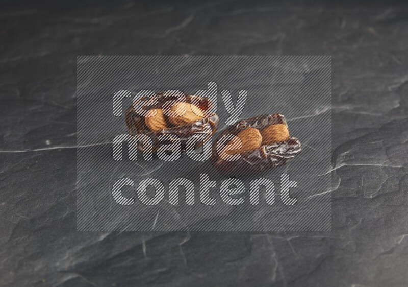 two almond stuffed madjoul dates on a black textured background
