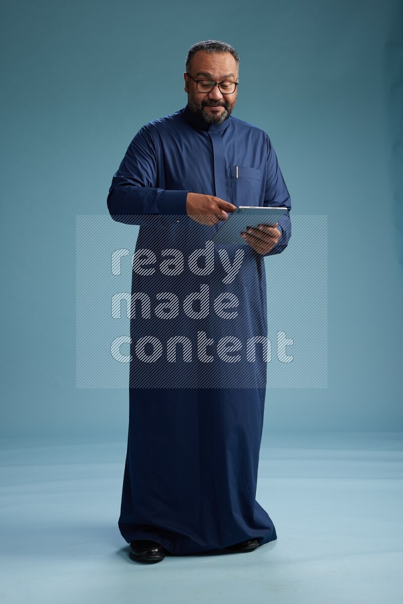 Saudi Man without shimag Standing working on tablet on blue background