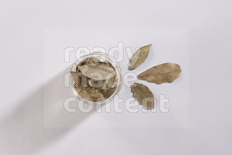 A glass jar filled with dried bay leaves on white flooring