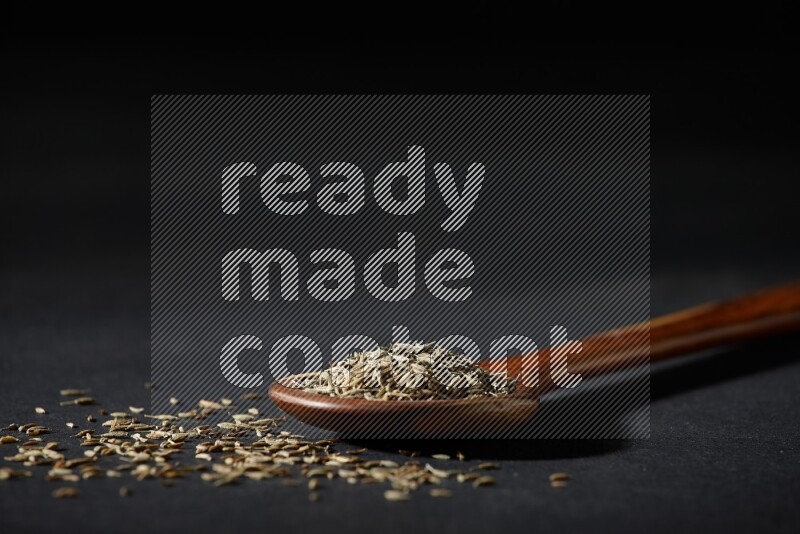 مغرفة خشبية ممتلئة بحبوب الكمون على خلفية سوداء