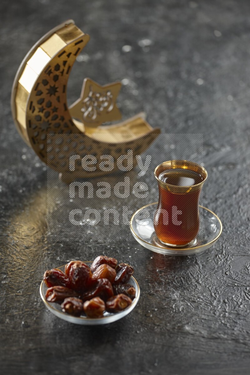A wooden golden crescent lantern with different drinks, dates, nuts, prayer beads and quran on textured black background