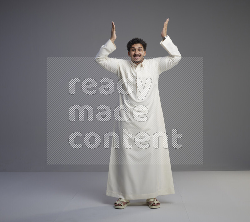 A Saudi man standing wearing thob interacting with the camera on gray background