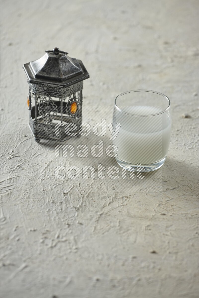 A silver lantern with different drinks, dates, nuts, prayer beads and quran on textured white background