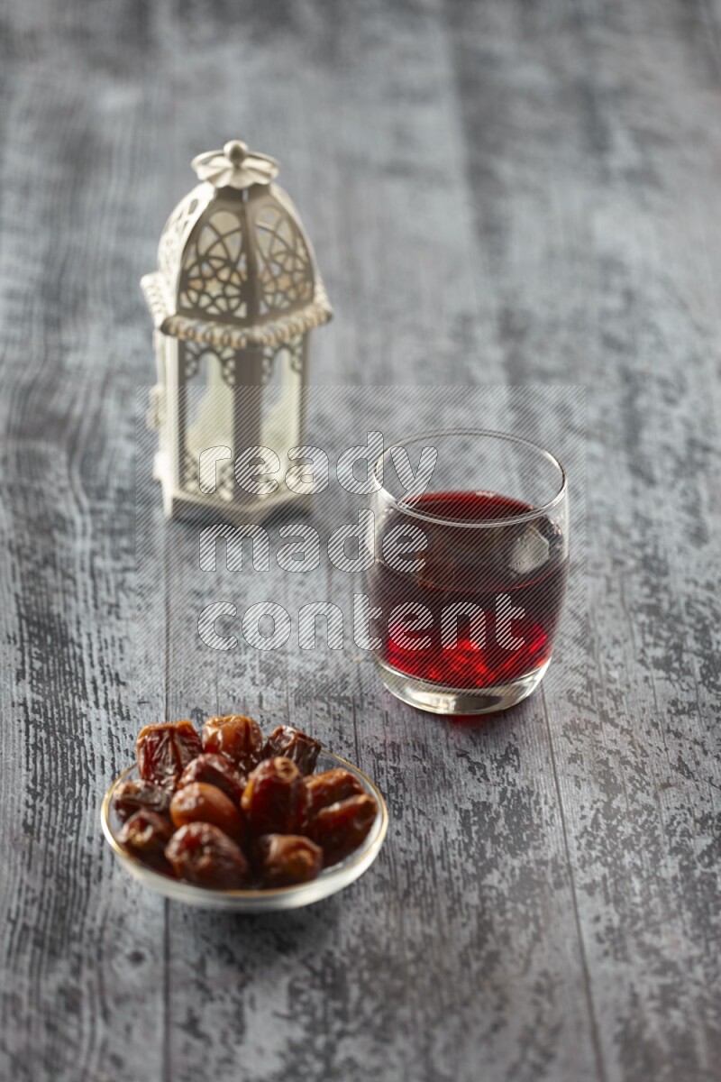 A white lantern with different drinks, dates, nuts, prayer beads and quran on grey wooden background