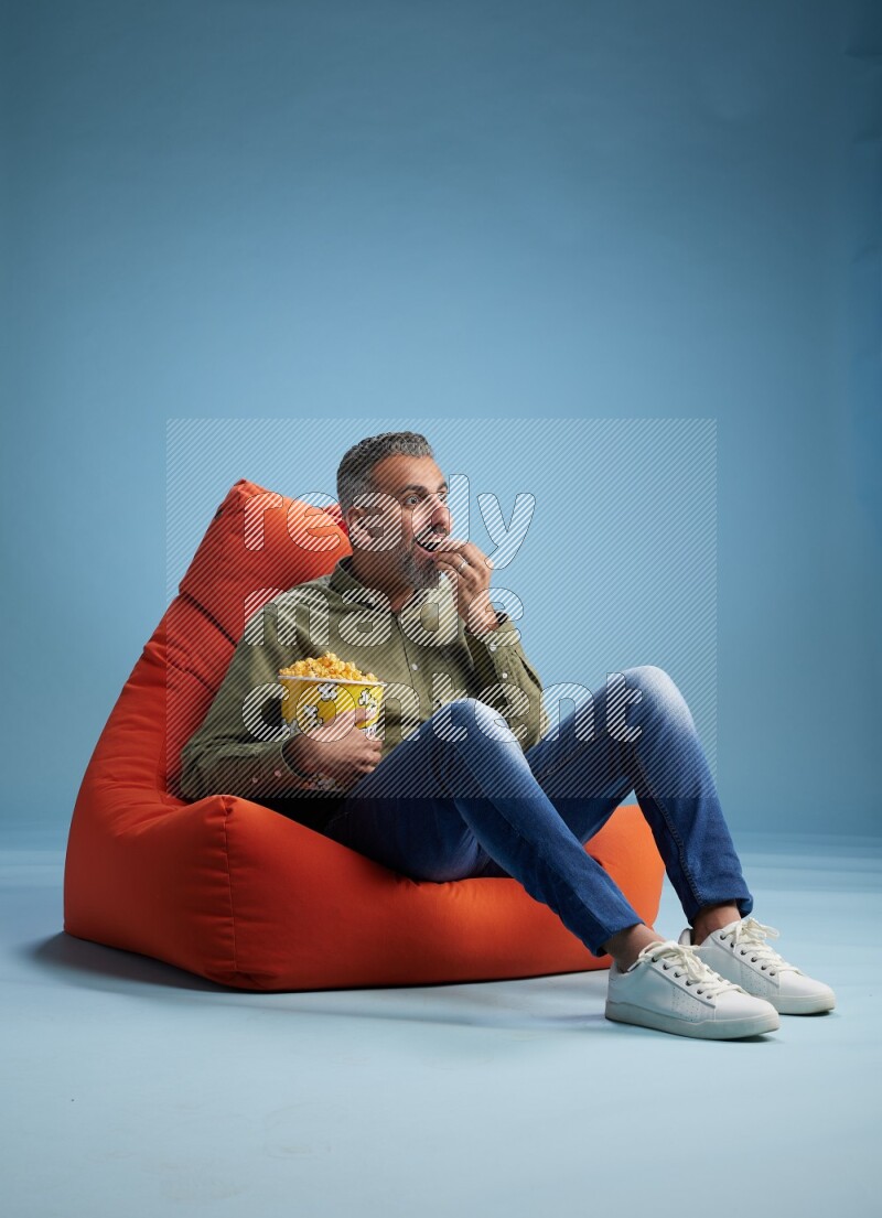 A man sitting on an orange beanbag and eating popcorn
