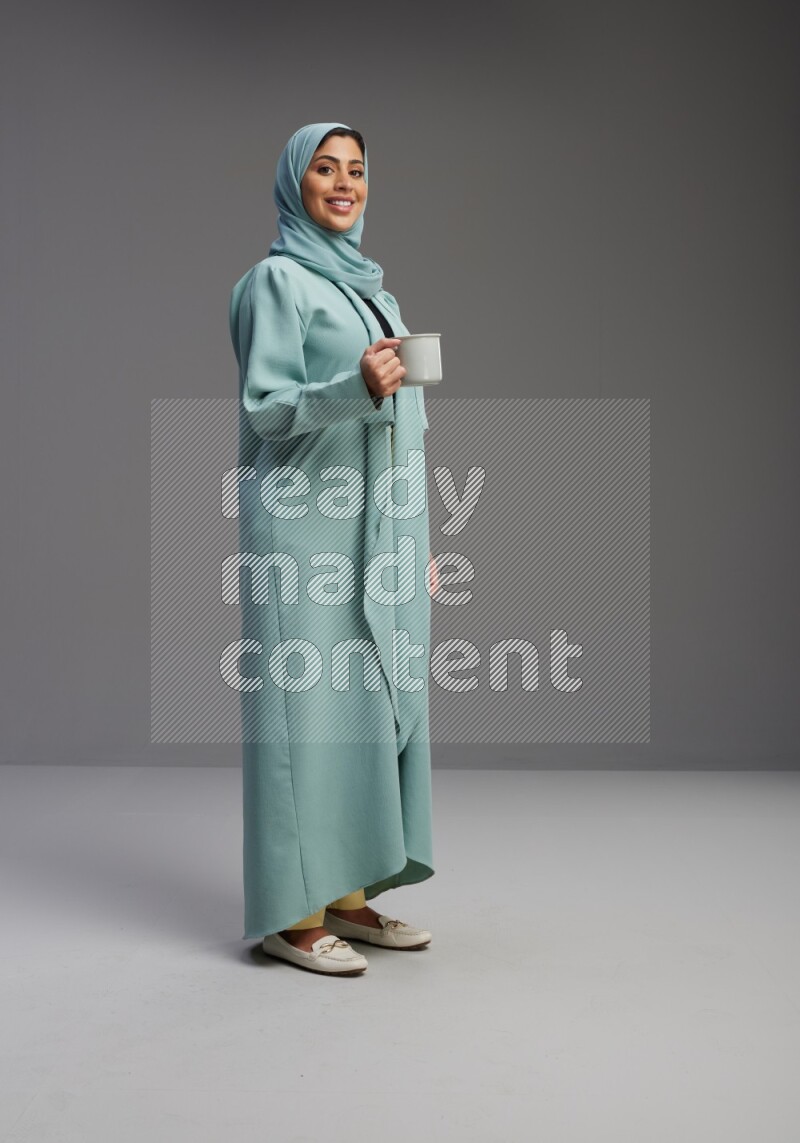 Saudi Woman wearing Abaya standing  holding a mug on Gray background