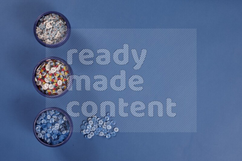 Multicolored pottery bowls full of colored buttons on blue background