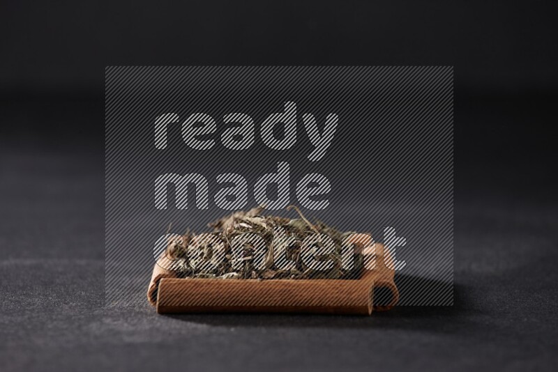 أربعة من أعواد القرفة مكونة شكل مربع بداخلها ريحان مجفف علي خلفية سوداء