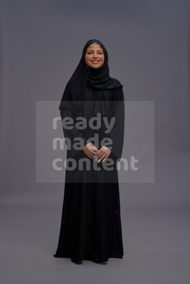 Saudi woman wearing Abaya standing interacting with the camera on gray background