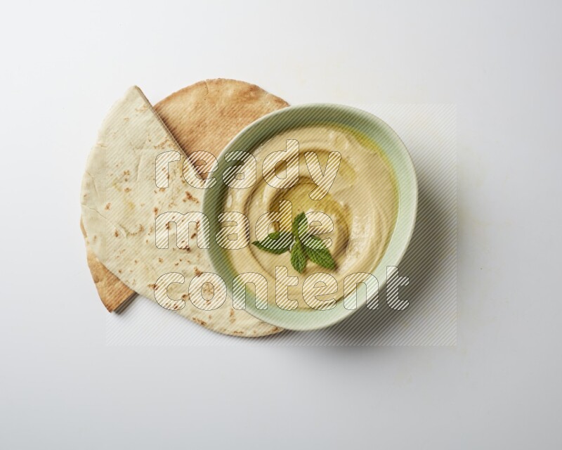 Hummus in a green plate garnished with mint on a white background