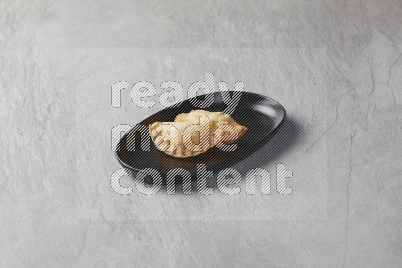 Two fried sambosas in an oval shaped black plate on a gray background