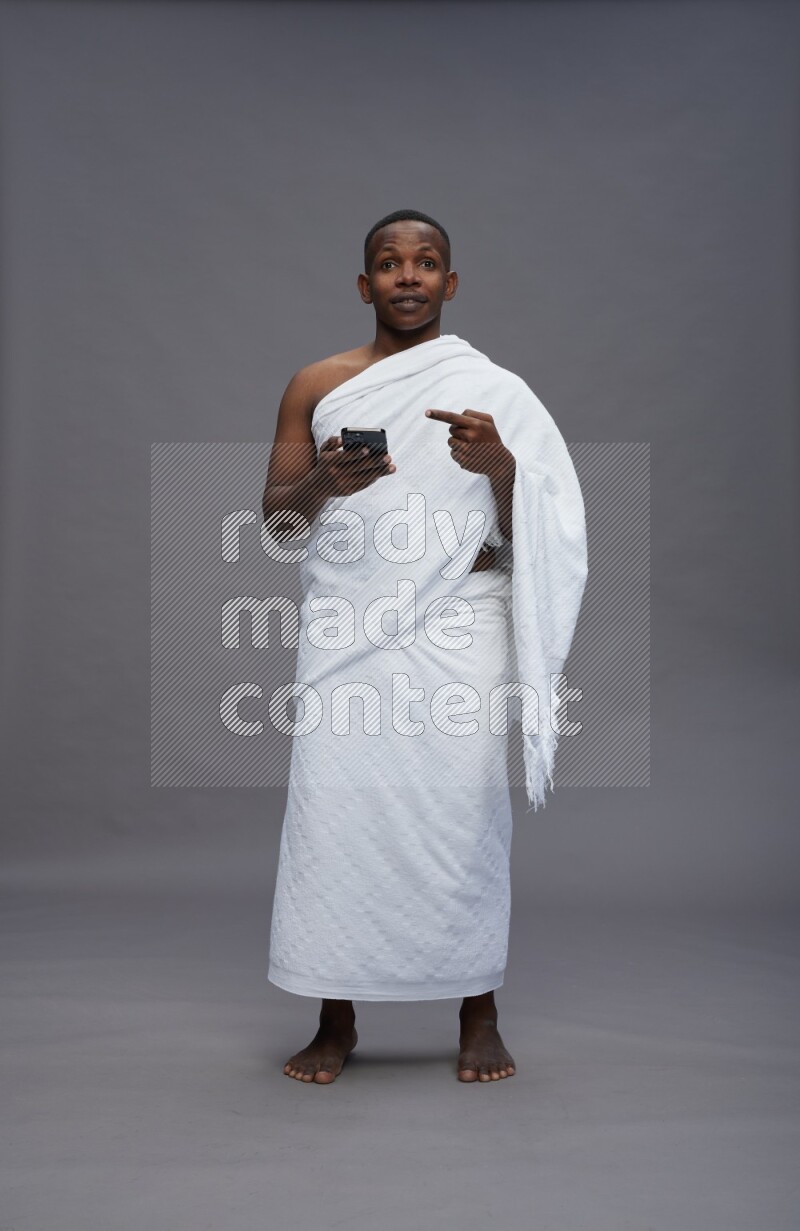 A man wearing Ehram Standing texting on phone on gray background