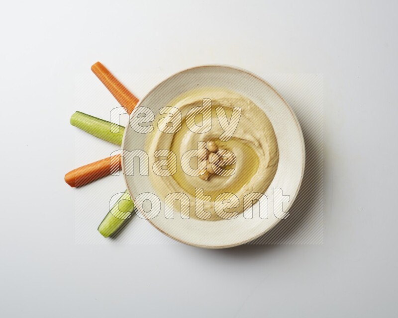 Hummus in a pottry plate garnished with roasted chickpeas on a white background