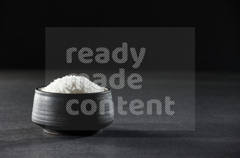 A black pottery bowl full of desiccated coconut on a black background in different angles
