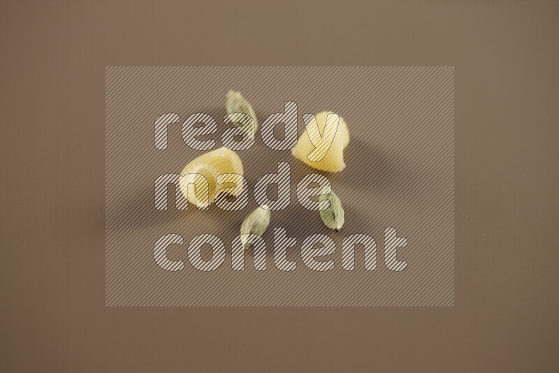 Raw pasta with different ingredients such as cherry tomatoes, garlic, onions, red chilis, black pepper, white pepper, bay laurel leaves, rosemary and cardamom on beige background