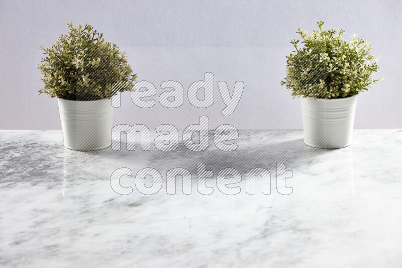 Two green artificial plants in white pot on grey marble background