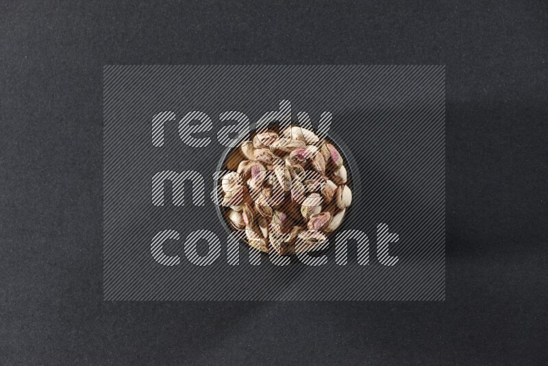 A black pottery bowl full of peeled pistachios on a black background in different angles