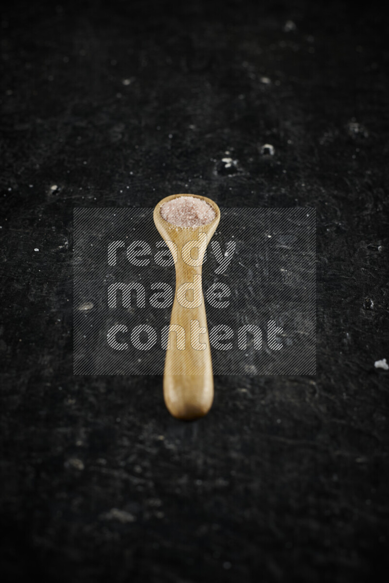 A wooden spoon full of pink himalayan salt on black background