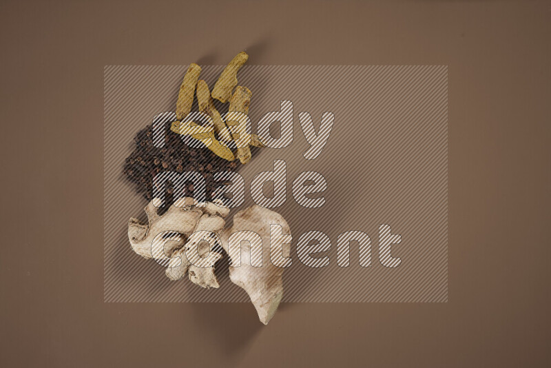 بهارات كاملة متنوعة تتضمن زنجبيل طازج ومجفف، أعواد قرفة، هيل، أصابع كركم، قرنفل، يانسون نجمي على خلفية بيج