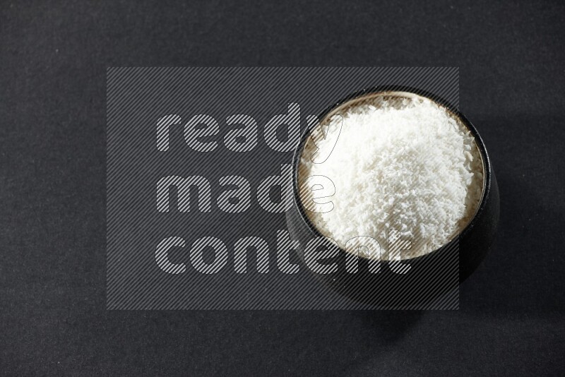 A black pottery bowl full of desiccated coconut on a black background in different angles